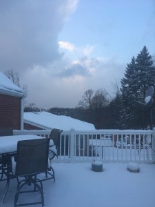 View of a snow-covered deck and partly cloudy sky.